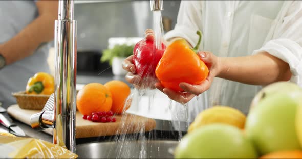 Couple preparing breakfast, rinsing peppers under kitchen sink