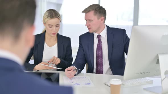 Focused Professionals Discussing Documents and Working on Tablet