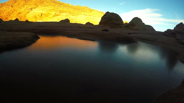 Gliding view over a frozen pool of water as the sun lights up the cliffs.