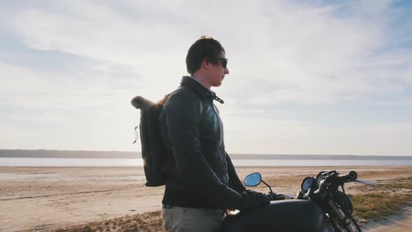 Motorcyclist Standing with His Motorbike on the Beach During Sunset