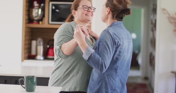 Caucasian lesbian couple smiling and dancing in kitchen