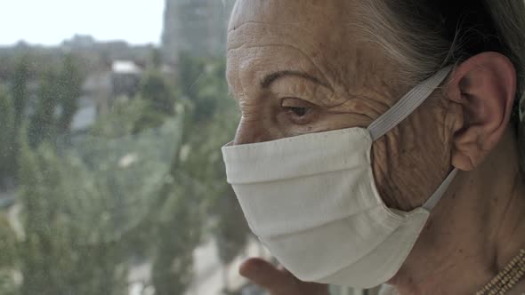 Older Woman in Face Mask Looks Through at the Window