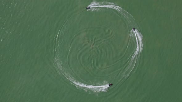 Three jet skis riding in a circle on lake, aerial top-down view, slomo