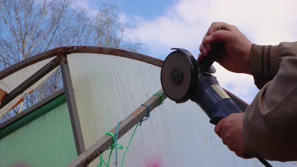 Hands with an Angle Grinder Cut a Rusty Metal Greenhouse