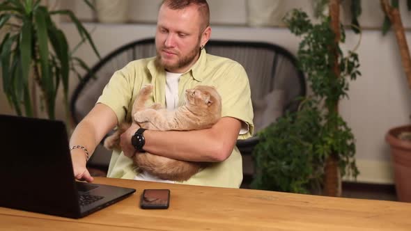 Man is working on a black notebook, laptop and cat is laying in his hand