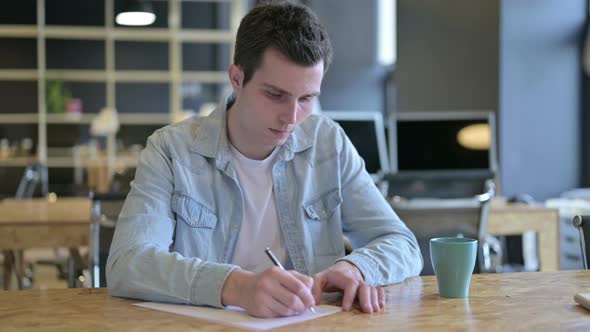 Hardworking Young Designer Reading Documents in Modern Office