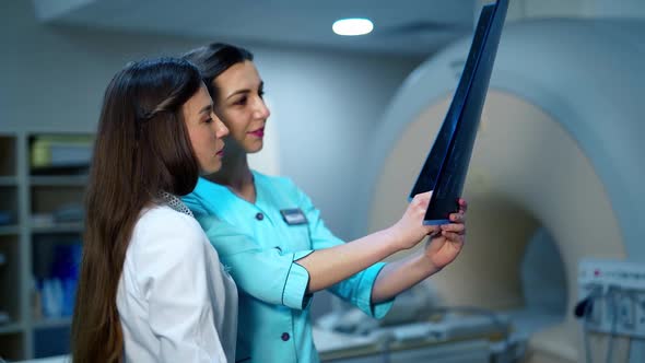 Female doctors analyzing x-ray together. Young women in medical uniform examining x-ray photo 