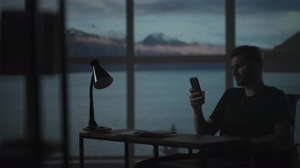 Silhouette of a Man Sitting at a Table Looking at a Mobile Phone Thinking and Analyzing the Stock