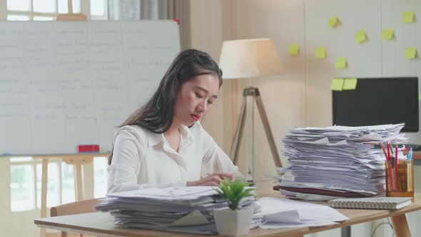 Asian Woman Writing Something On Paper While Working With Documents At The Office