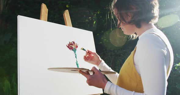 Caucasian woman with brown hair painting in sunny garden