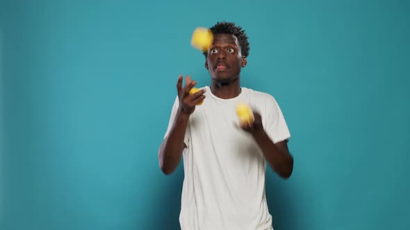 Playful Adult Juggling Lemons and Standing Over Blue Background