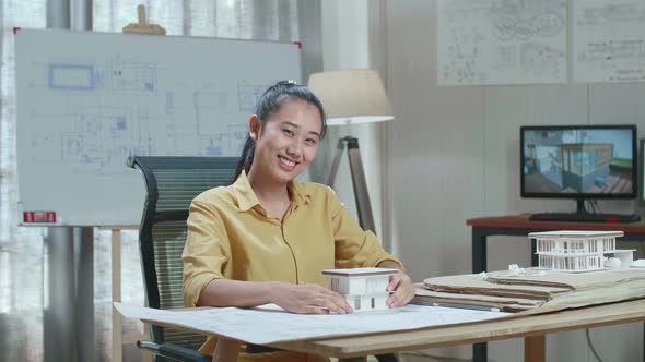 Asian Woman Engineer Holding Paper Model Of House Warmly Smiling To Camera At The Office