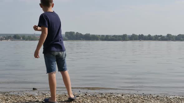 Teenage Boy in Shorts and Tshirt Throws Stones Into the River