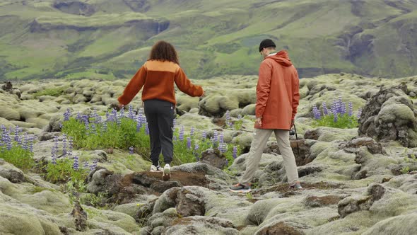 Couple Hiking Over Rocks In Mossy And Wildflower Landscape