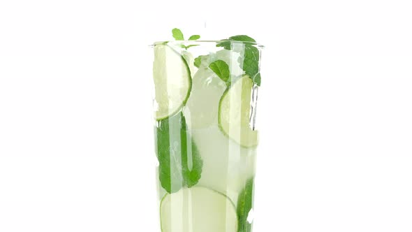 pour water in glass with with lime, mint and ice on white background. refreshing drink lemonade