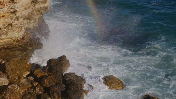 Sea waves breaking against cliff viewed from above.