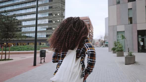 Back View of African American Girl with Curly Hair in Card Shirt is Going Home From the University