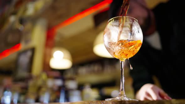 A Professional Bartender is Preparing an Alcoholic Cocktail with Ice Cubes to Customers at the Bar