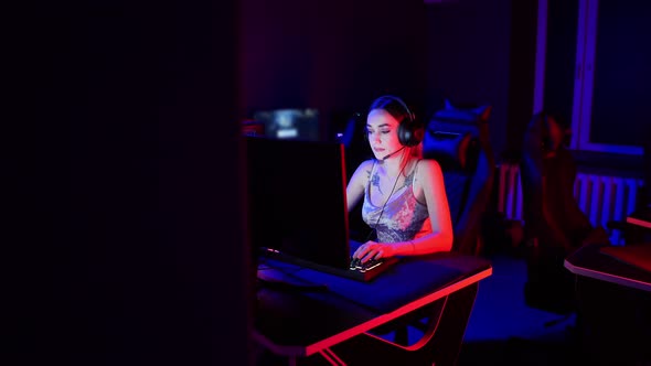 Gaming Concept - Young Attractive Woman with Tattoos Sits in the Chair in Neon Gaming Club and