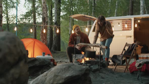 Couple Cooking Food over Campfire in Evening