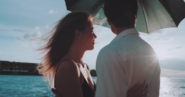 Woman smiles toward man holding umbrella by the Sea