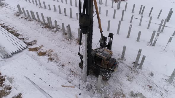 Aerial drone view of a pile bore machine and worker at winter construction site 04