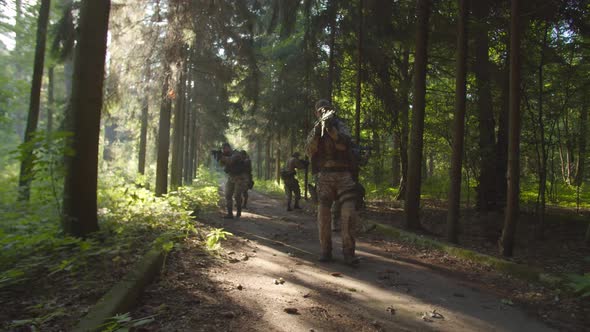 Group of Armed Soldiers Moving on Path Along Dense Forest at Daybreak