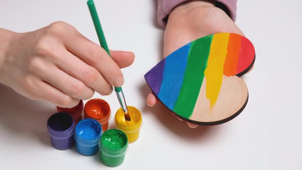 Hand Paints a Wooden Heart in Colors of Gay Pride Flag