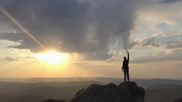 Drone Shot of a Silhouette of a Mountaineer Standing on Top of a Mountain and Victoriously Raising