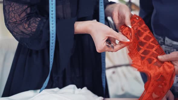 Professional dressmaker is cutting red lace with scissors with the help of a tailor in atelier