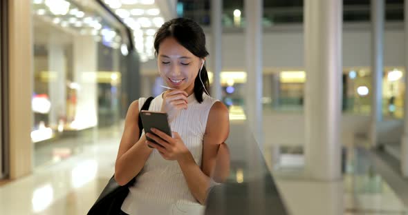 Woman using smart phone and holding paper bags in shopping mall 