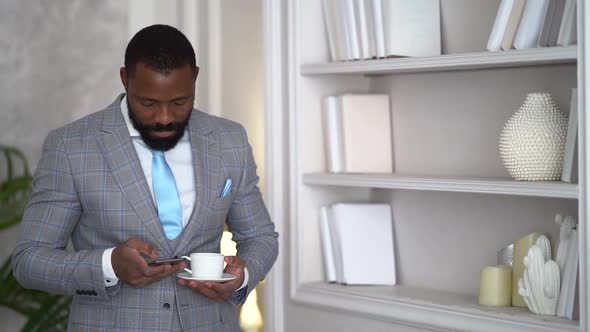 Cheerful Afro American Businessman Is Calling By Mobile Phone, Drinking Coffee in Living Room