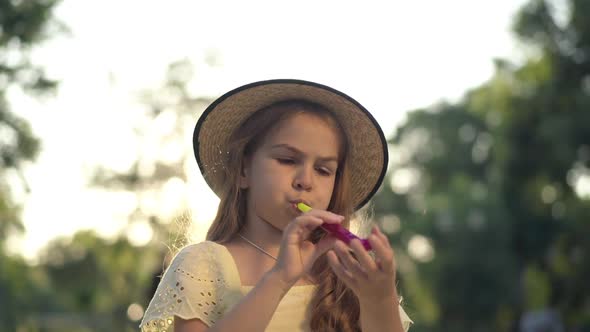 Pretty Cute Girl Blowing Party Whistle Sitting in Sunrays Outdoors