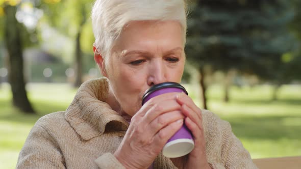 Happy Elegant Grandmother of Retirement Age Sitting on Park Bench Drinking Tea