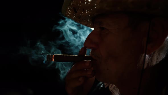 The man smokes a cigar. An elderly farmer in a straw hat smokes a cigar outside the ranch