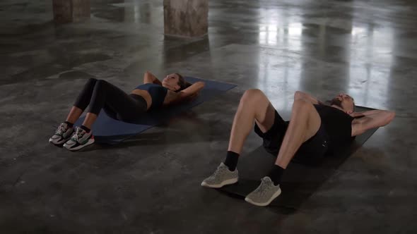 Young Stylish Man and Woman in Sportswear Workouting at Empty Studio Doing Synchronous Crunches