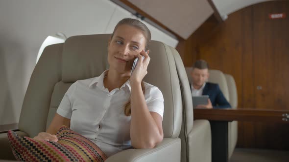 Attractive Businesswoman Smiling While Talking By Selphone with Her Friend in Business Jet