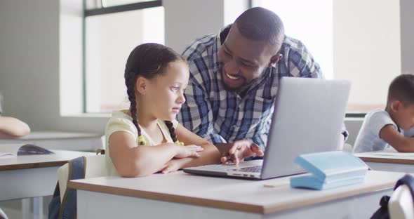 Video of happy african american male teacher helping caucasian girl with laptop