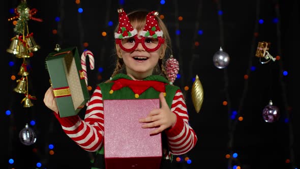 Kid Girl in Christmas Elf Santa Helper Costume with Present Gift Box Looking Inside