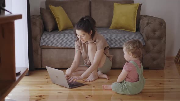 Mother Multitasking Holding Baby Infant and Using Computer Laptop at Home