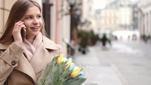 Pretty Young Woman Holding Bunch of Tulips Using Smartphone in Public Place