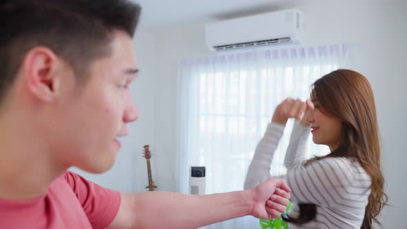 Asian young loving couple dance with music together in living room.