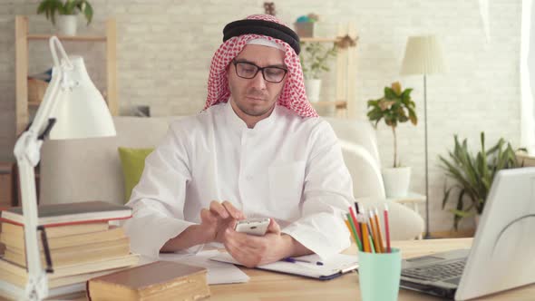 Arab Man Sitting at the Table and He Uses a Smartphone