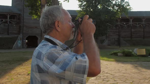 Pensioner Holds Black Camera and Takes Photo in Museum Park