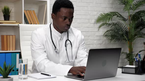 African American Man Doctor Typing Text on Keyboard Laptop in Clinic Office