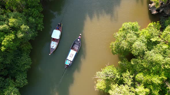 top down aerial drone of two wooden Thai longtail boats pass each other on the river surrounded by m