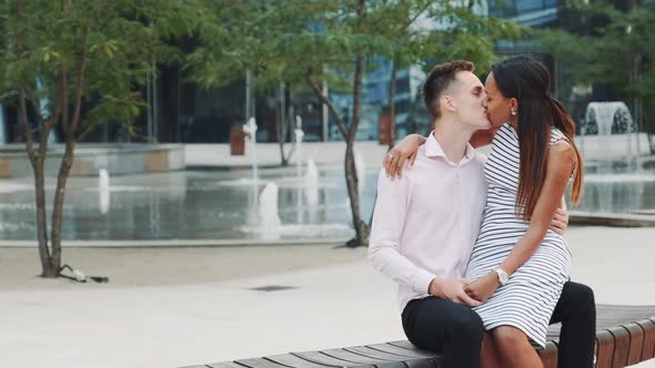 Two Mixed-race Lovers Sitting on a Bench and Kissing