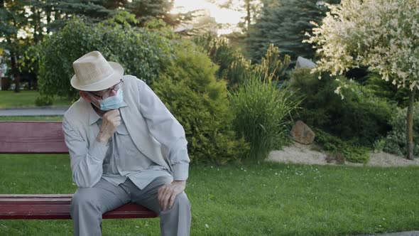 The Senior Man in Medical Mask Sitting Thoughtfully on Bench in Summer Park