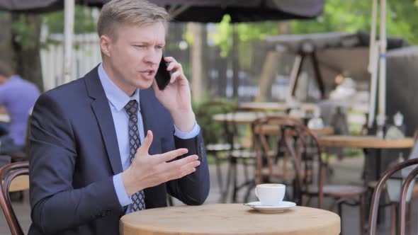 Businessman Reading Book While Sitting in Outdoor Cafe