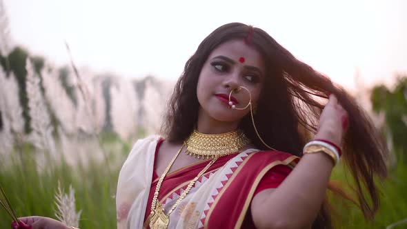 A newly wed cheerful and playful Indian woman plays with her beautiful curly long hair in a field ou